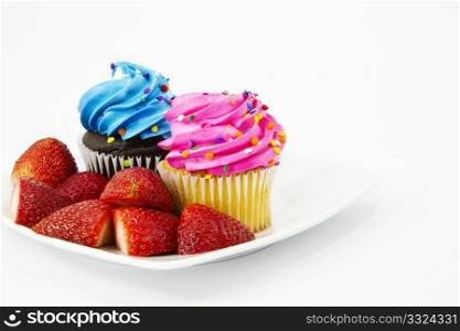 Two cupcakes, one with blue frosting and one with pink frosting, are garnished with sliced strawberries