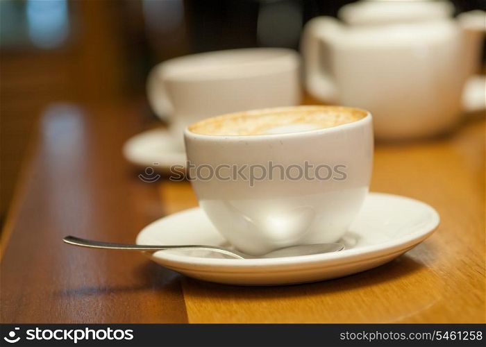 Two cups of cappuccino on a table and white teapot on background