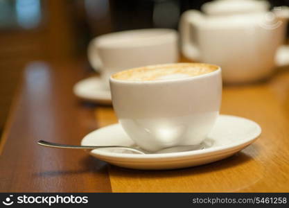 Two cups of cappuccino on a table and white teapot on background