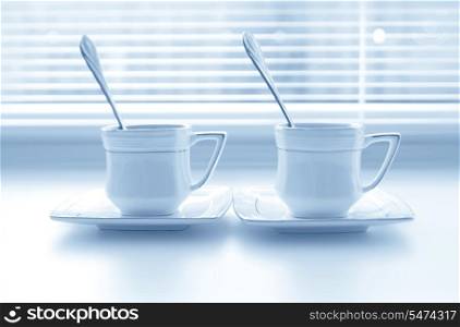 Two cups of coffee on the white windowsill with shutters