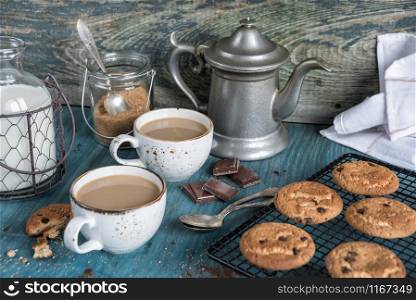 Two cups of coffee with milk and homemade oatmeal cookies with chocolate on a blue wooden vintage table, rustic style, low key