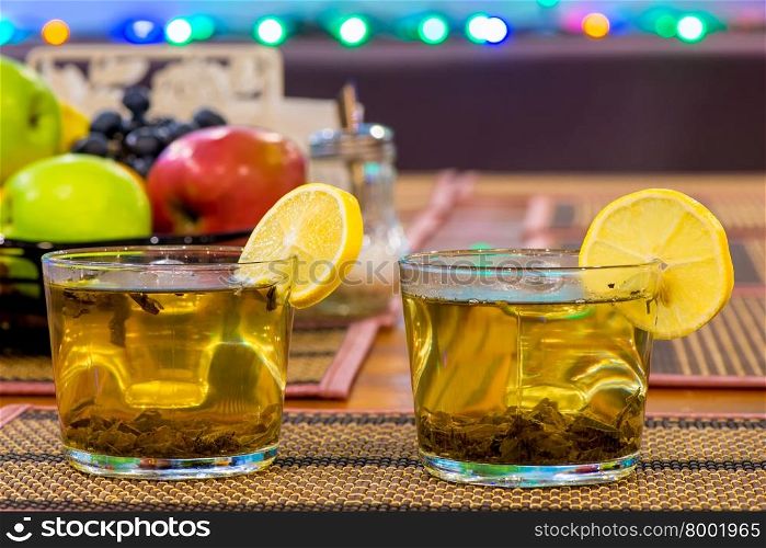two cups of green tea with lemon and fruit on the table