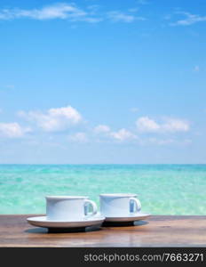 Two cups of hot coffee over a clear ocean’s water