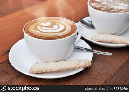 two cups of latte art coffee in a white cup on wooden background