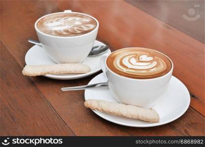 two cups of latte art coffee in a white cup on wooden background