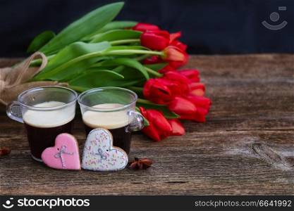 Two cups of Valentines day coffee with fresh red tulips  on wooden table with copy space. Valentines day coffee