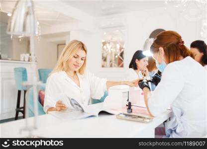 Two customers on manicure procedure in beauty salon. Professional beautician and female customers, nail care in spa studio, fingernail treatment