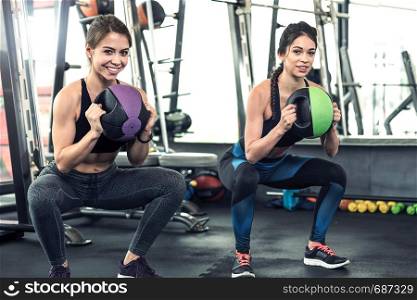 Two cute athletic girls have a hard workout at the gym, doing weight squats