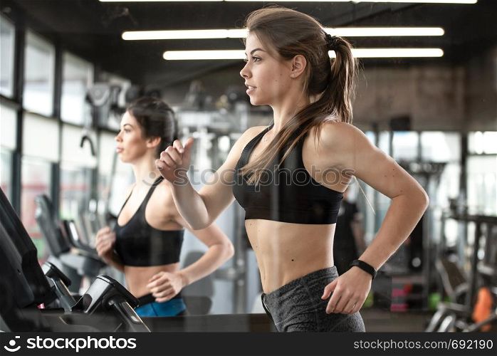 Two cute girls are doing heavy sports training and running on the treadmill in the gym.