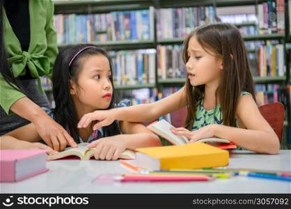 Two cute girls conflict while reading books in library when teacher teaching. People lifestyles and education. Young friendship and Kids relationship in school concept. Daycare theme