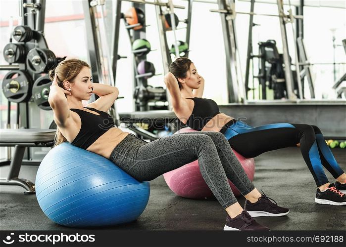 Two cute girls doing heavy athletic workout in the gym doing exercises for abdominal muscles
