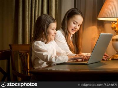 Two cute girls sitting at table and using laptop