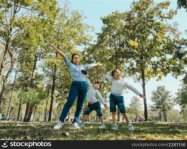Two cute little Asian girls in summer outfits, having fun with a beautiful young mother smiling happily in the park. Motherhood and family concept.