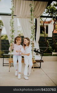 Two cute little girls on the swing in the house backyard