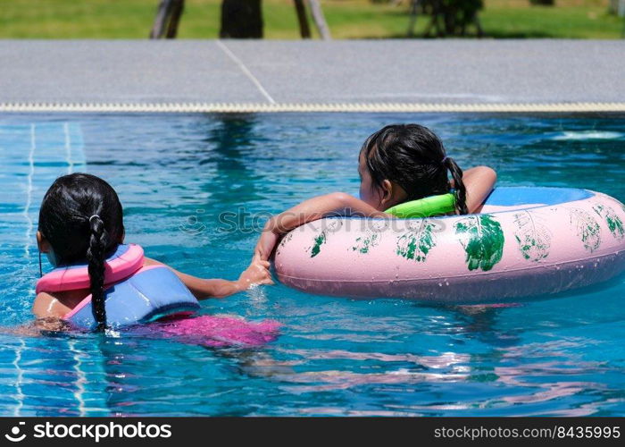 Two cute little girls playing in the pool. Smiling sisters are swimming in life jackets in the pool on a sunny day. Summer lifestyle concept.