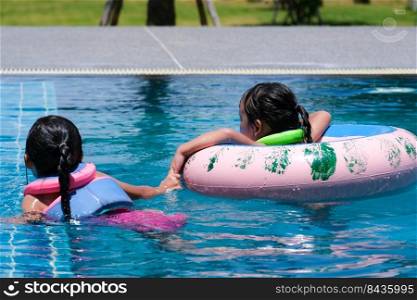 Two cute little girls playing in the pool. Smiling sisters are swimming in life jackets in the pool on a sunny day. Summer lifestyle concept.
