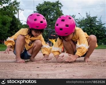 Two cute little sisters in helmets are playing with sand in park on a sunny summer day, taking a break after cycling practice. develop imagination and exploration.