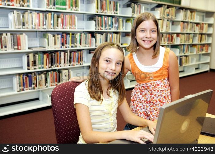 Two cute school girls doing research in the school library.