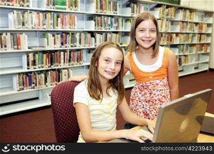 Two cute school girls doing research in the school library.