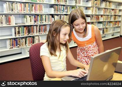 Two cute school girls doing research online in the school library.