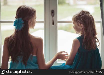 Two cute sisters looking behind the window