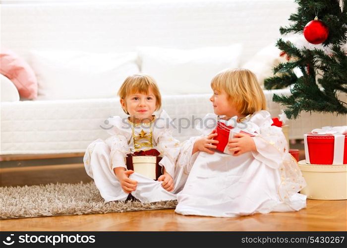 Two cute twins girl sitting with presents boxes near Christmas tree