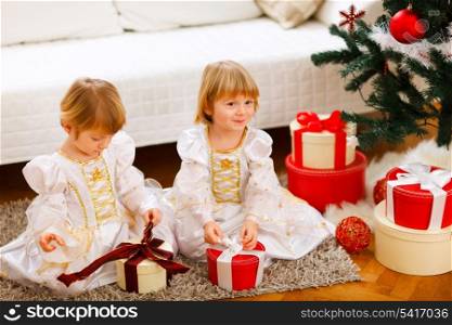 Two cute twins girls opening presents near Christmas tree