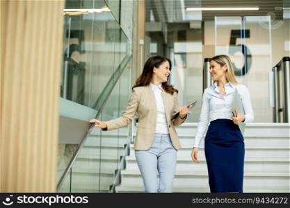 Two cute young busi≠ss women walking on stairs in the office hallway