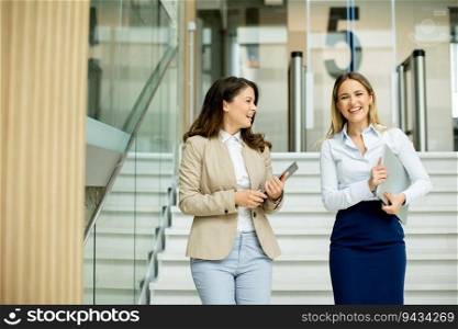 Two cute young business women walking on stairs in the office hallway