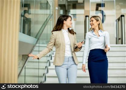 Two cute young business women walking on stairs in the office hallway