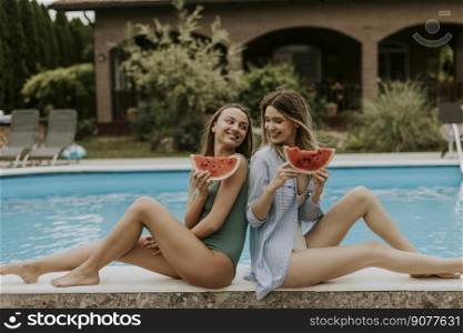 Two cute young women sitting on by the swimming pool and eating watermelon in the house backyard