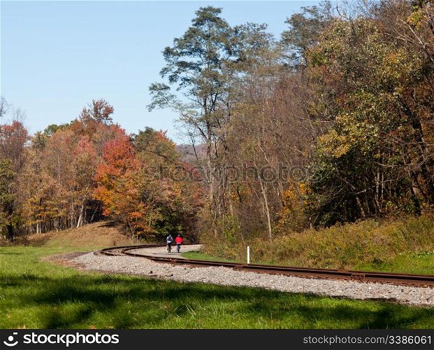 Two cyclists ride bikes down besides old railway line in rural countryside