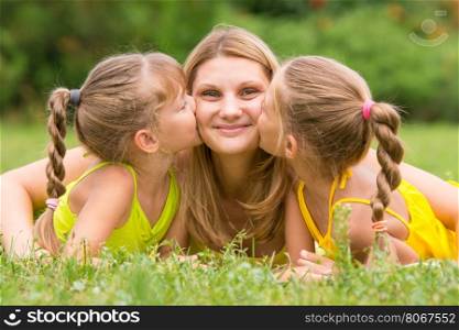 Two daughters kissing mother lying on the grass on a picnic