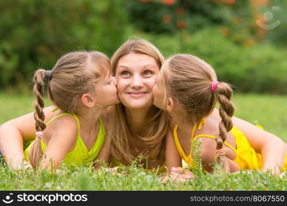 Two daughters kissing mother lying on the grass on a picnic, Mother looked up fun