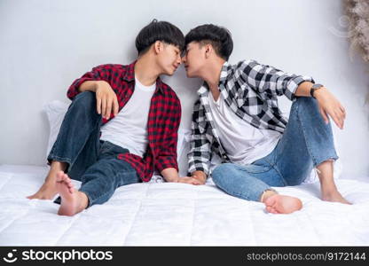 Two dear young men were sitting on the bed, holding hands and looking at each other.