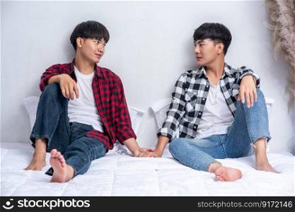 Two dear young men were sitting on the bed, holding hands and looking at each other.