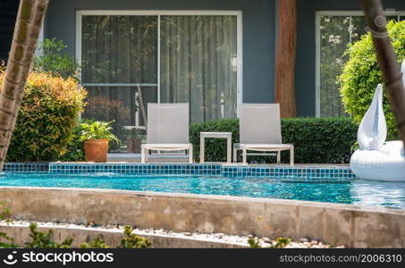 Two deck chairs and table beside outdoor swimming pool in resort hotel for vacation travel leisure