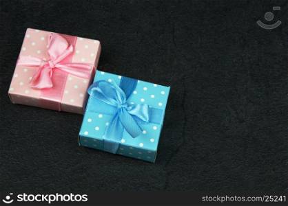 Two decorative Christmas gift boxes, tied with pink and blue ribbons, on a dark stone background. Flat, horizontal view from the top.