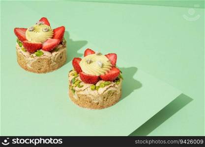 Two delectable desserts topped with fresh strawberries sitting on a plain white background. Two desserts covered in strawberries sit on a piece of white paper