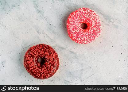 Two delicious donuts with chocolate and strawberry icing sprinkled on top with spicy crumbs closeup on a gray concrete surface. Confectionery sweets for breakfast, image with copy space.. Delicious chocolate donuts on a gray concrete surface.