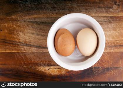 Two different eggs in a small bowl on a chopping board from above
