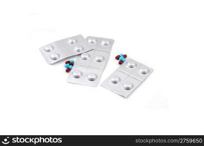Two different kind of prescription medication, one a blue and burgundypill, the other one sealed in silver folia, on white background.