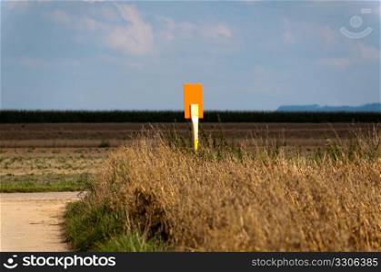 Two dirt ways meeting out in the fields with sign shining brightly in the sunlight