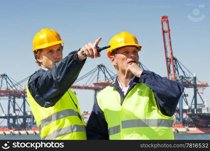 Two dockers in discussion, in front of a large industrial harbor