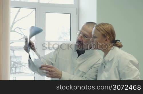 Two doctors analyzing and comparing x-ray images in the clinic. Experienced man giving extensive consultation to a young female doctor or student