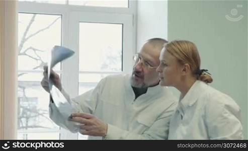 Two doctors analyzing and comparing x-ray images in the clinic. Experienced man giving extensive consultation to a young female doctor or student