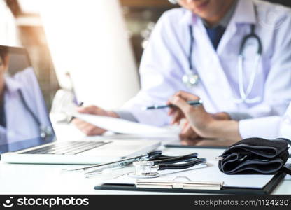 Two doctors being discussing patient history in an office pointing to a clipboard with document paper as they make a diagnosis or recommend on treatment.