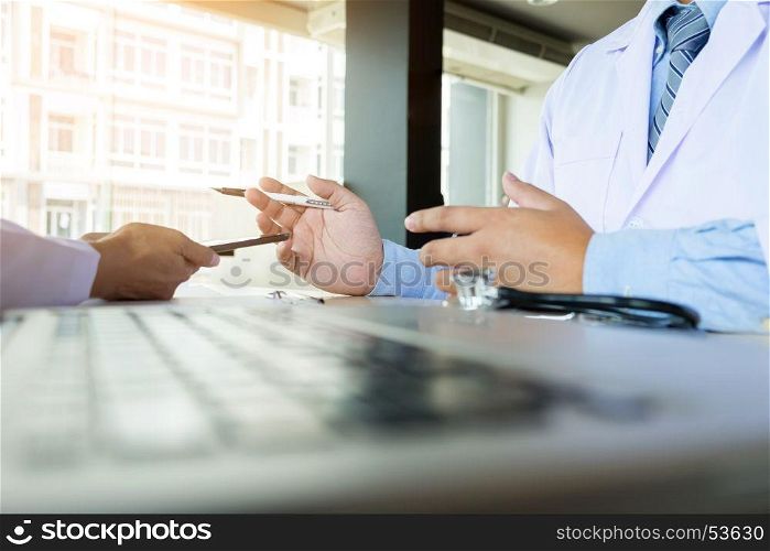 Two doctors discussing patient notes in an office pointing to a clipboard with tablet as they make a diagnosis or decide on treatment.
