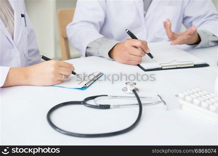 Two doctors discussing patient notes in an office pointing to a clipboard with paperwork as they make a diagnosis or decide on treatment.