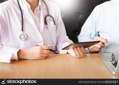 Two doctors discussing patient notes in an office pointing to tablet as they make a diagnosis or decide on treatment.